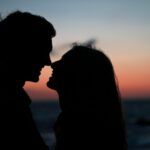 silhouette of man and woman about to kiss on beach during sunset